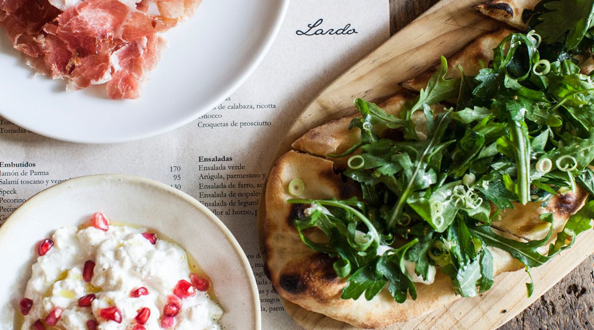 Flatbread with greens, cheese and cured ham on the table at Lardo